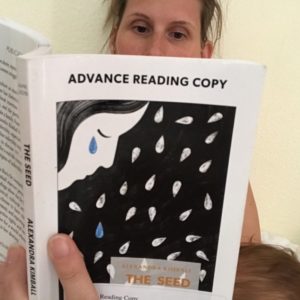 Close-up of the cover of an Advance Reading Copy of "The Seed" by Alexandra Kimball. The book shows an illustration of a person with long hair crying against a dark background with tear-shaped seeds. The person reading the book in the photo is me. Peeping above the book is most of my nose and my eyes, which are turned downward towards the page. My fingers clasp the book open. You can glimpse a young baby, cradled in the arm of the hand that holds the book. From the position of the brown-haired head, you can tell is breastfeeding.